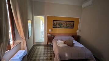 A hotel room with a bed, a nightstand, a lamp, a painting on the wall, and a patterned floor.