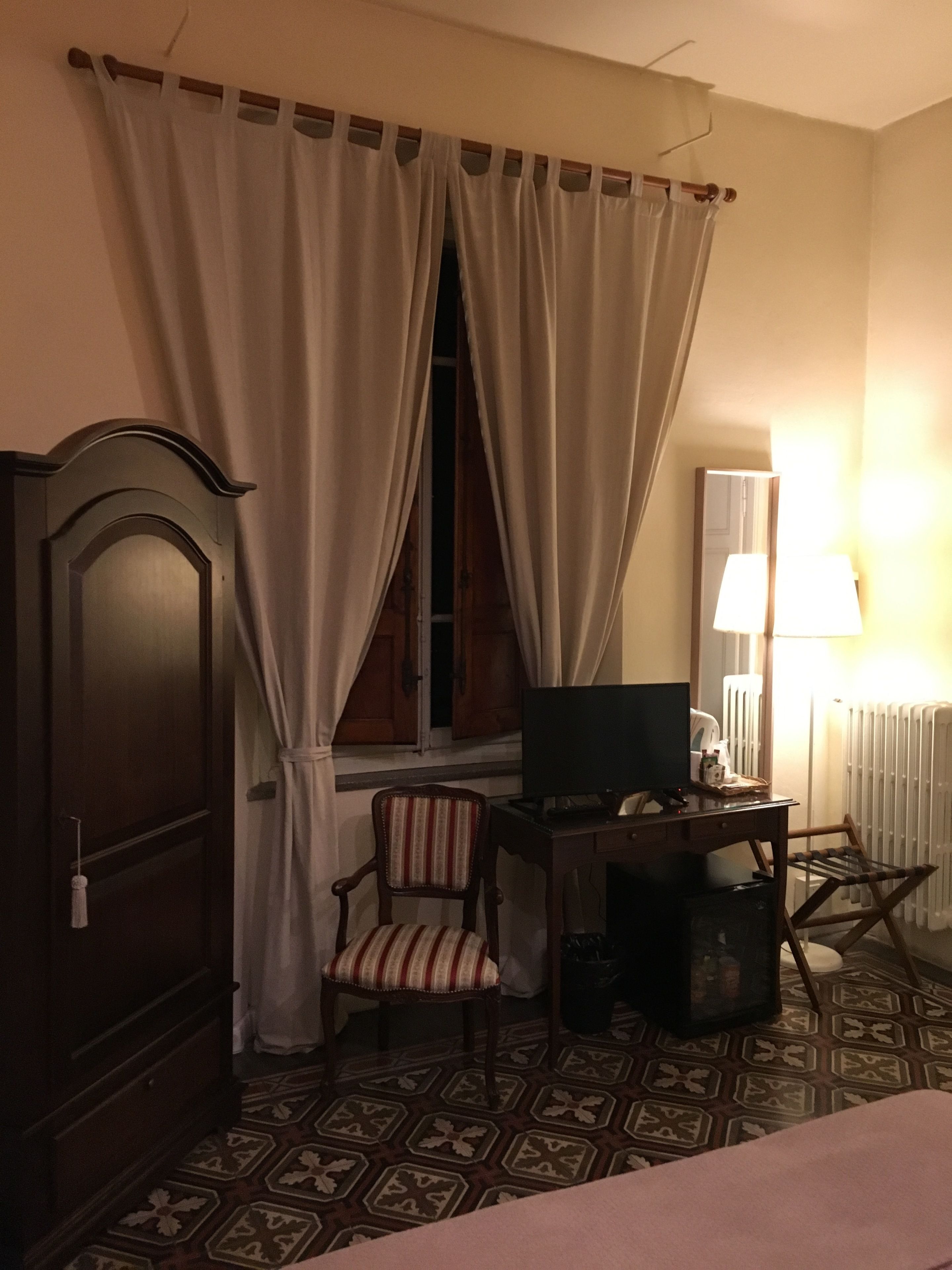 Ein Hotelzimmer mit Bett, Schreibtisch mit Computer, Stuhl, Kleiderschrank und Fenster mit Vorhängen.