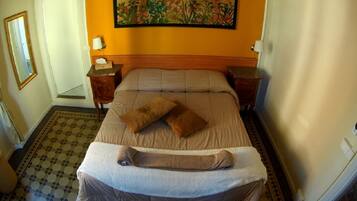 A hotel room with a bed, two bedside tables, a nightstand, a painting on the wall, and a patterned floor.