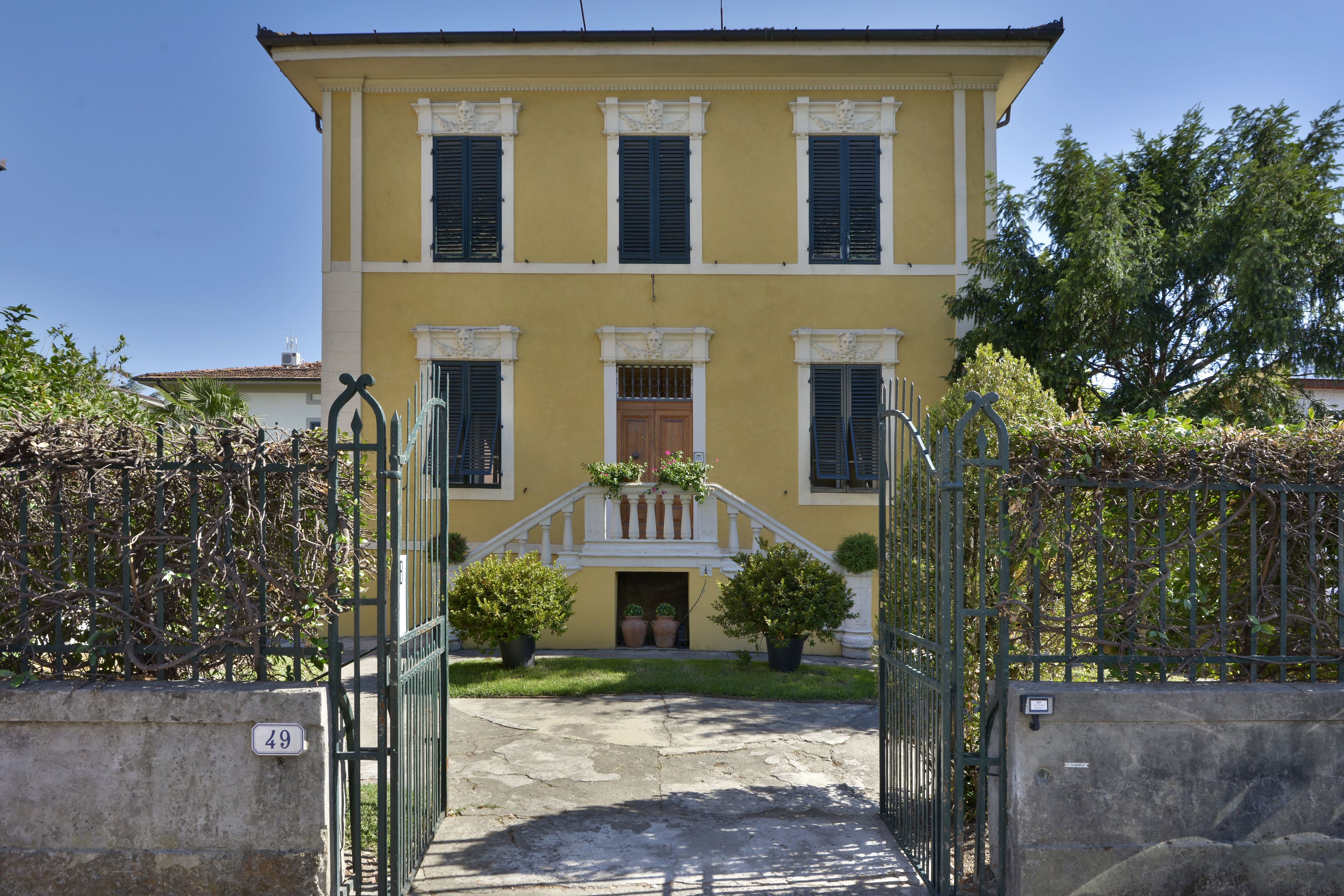 A yellow building with a central entrance, potted plants, and a metal gate.