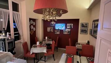 A dining area with red chairs and tables, a red ceiling lamp, and a television on the wall.