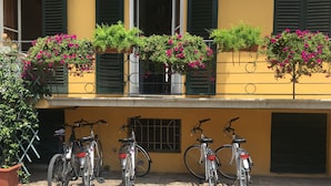 A building with a yellow facade, green shutters, and multiple bicycles parked in front. - Lucca in Villa San Donato (Lucca)
