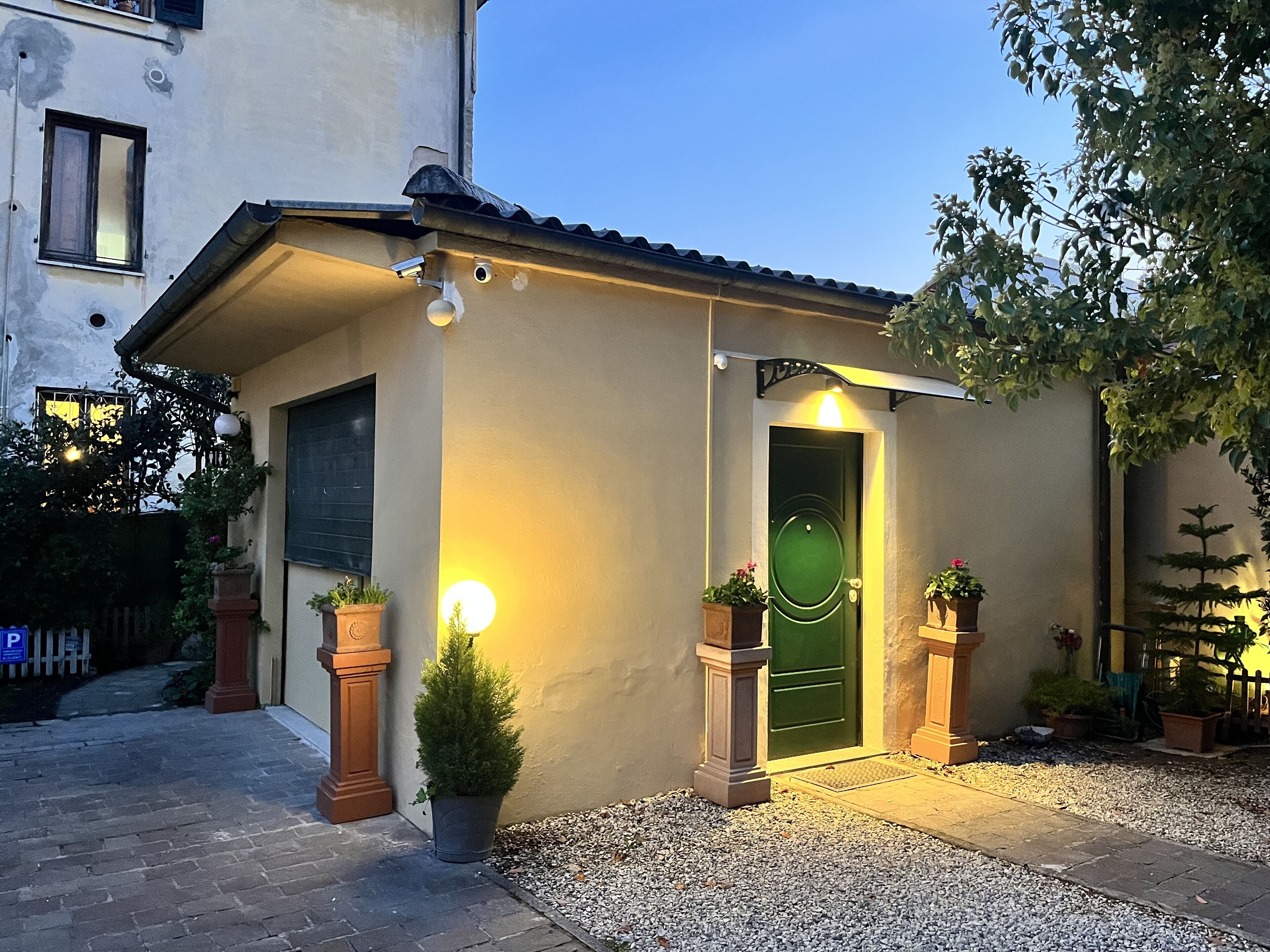 A small building with a green door, two potted plants, and a light fixture on the wall.