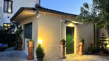 A small building with a green door, two potted plants, and a light fixture on the wall.