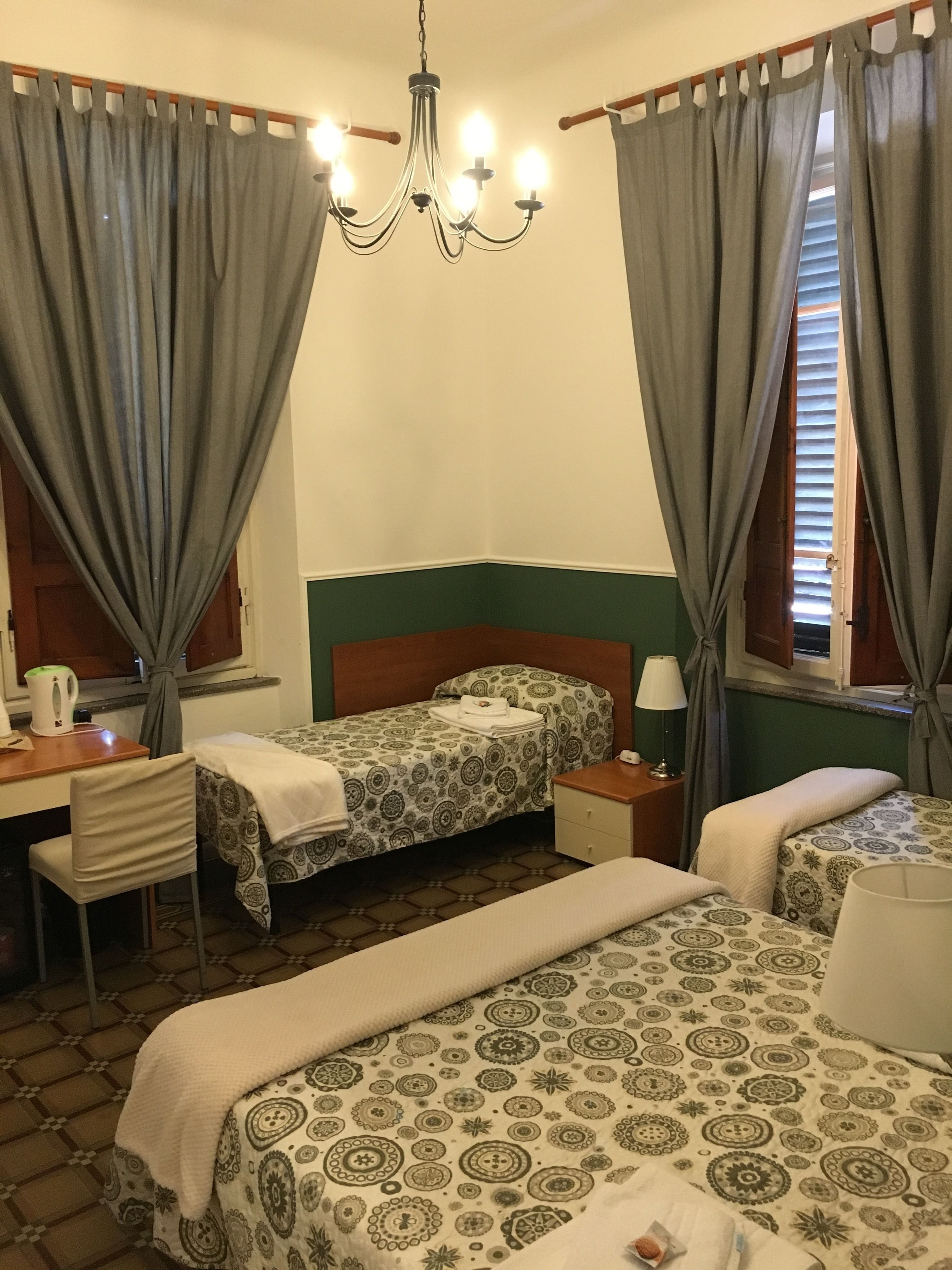 A hotel room with two beds, a desk, a chair, a nightstand, and a chandelier.