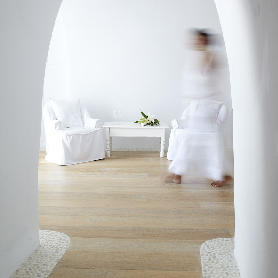 A minimalist room with a white chair, a small table with a floral arrangement, and a white dress on the floor.