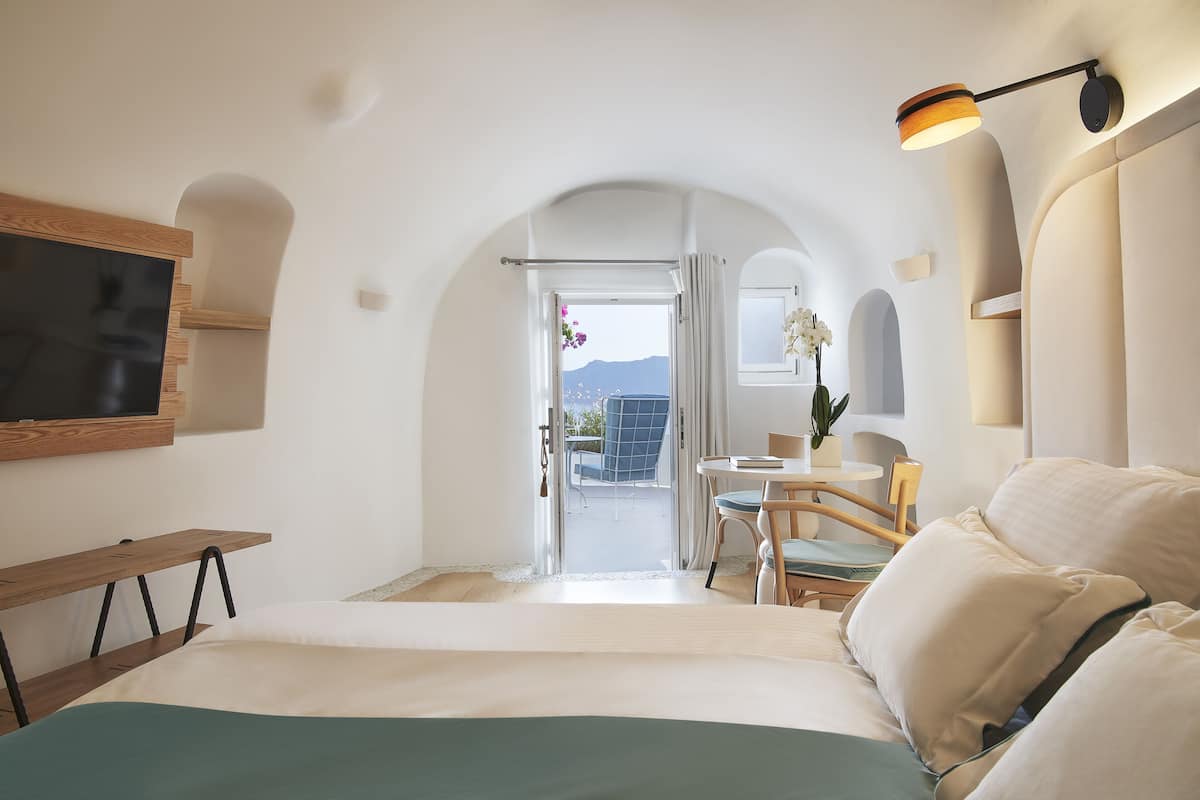 Habitación de hotel con cama, escritorio, silla, televisión y balcón con vistas a las montañas.