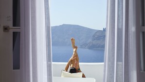 A person reclining on a white chair with a view of the sea and a mountain in the background. - Katikies Santorini – Gea House – The Leading Hotels of the World (Santorini)
