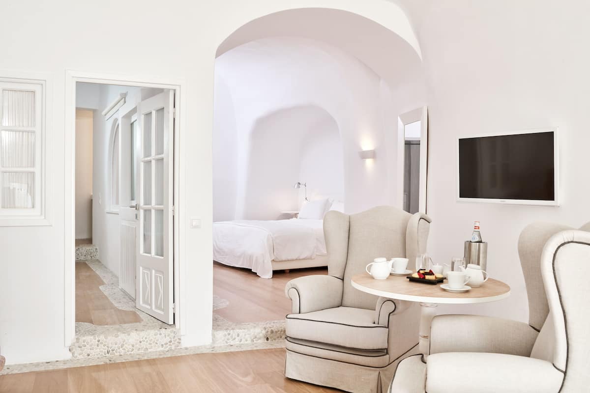 Ein modernes Hotelzimmer mit Bett, zwei Sesseln, einem kleinen Tisch mit Teeservice und einem an der Wand befestigten Fernseher.