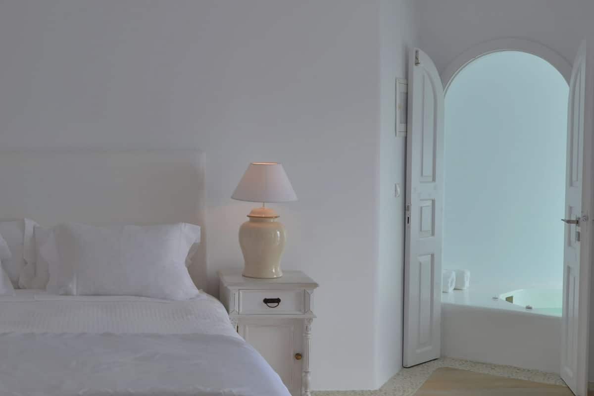 Ein helles Schlafzimmer mit einem Bett, zwei Nachttischen mit Lampen und einer Tür zu einem Badezimmer mit einer Badewanne.
