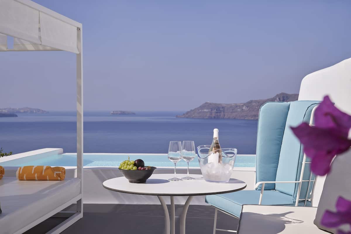 Eine Terrasse mit Meerblick, ein Tisch mit Obstschale, Gläsern und einer Flasche.