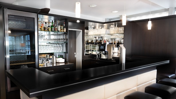 A bar area with a black countertop, bar stools, and shelves stocked with bottles and glasses. - eXo Individual Hotel Heilbronn (Heilbronn)