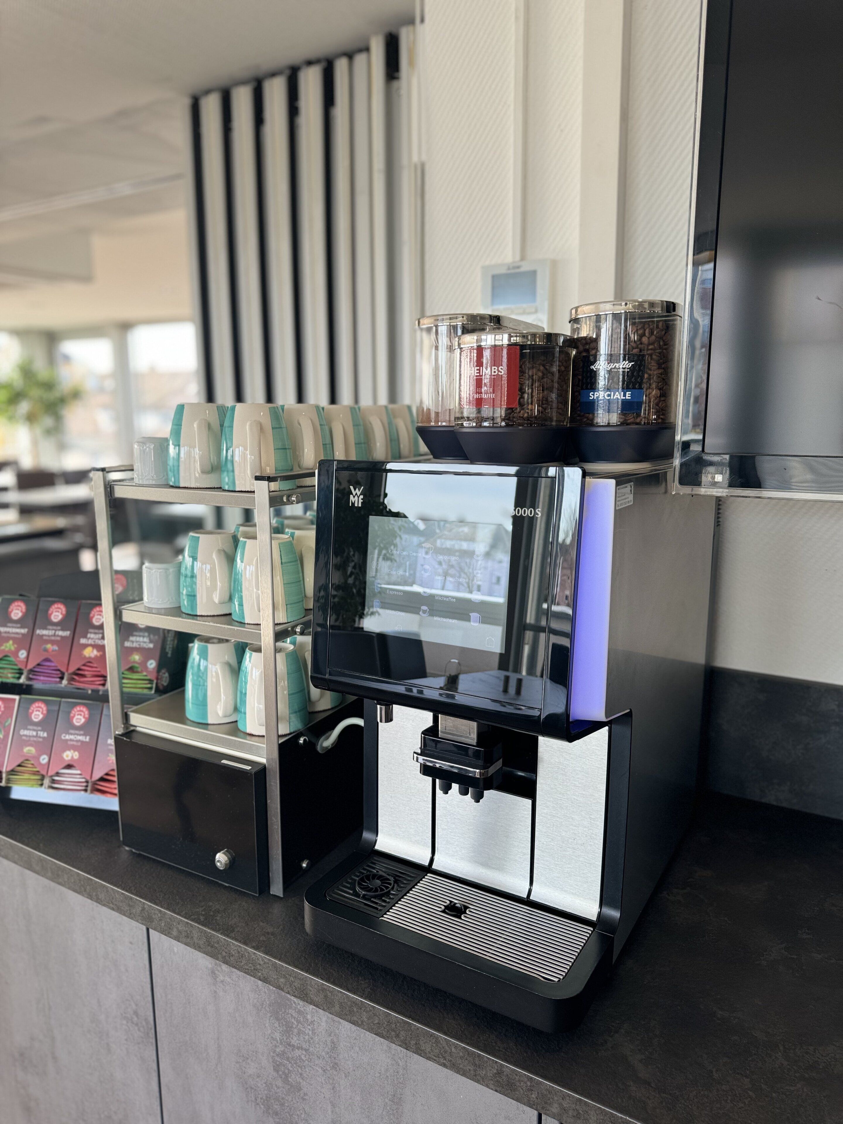 Una cafetera con varios pods de café y una pantalla digital, sobre una encimera de diseño moderno.