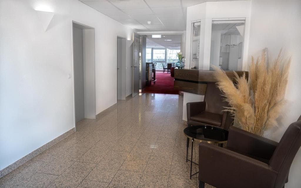 A hotel lobby with a red carpet, a reception desk, and a seating area with chairs and a table.