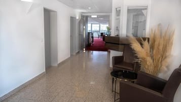 Un hall de hotel con alfombra roja, un mostrador de recepción y un área de descanso con sillas y una mesa.