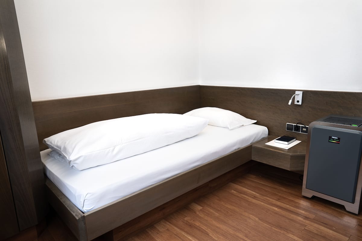 A single bed with white linens in a corner room with wooden flooring and a small bedside table.