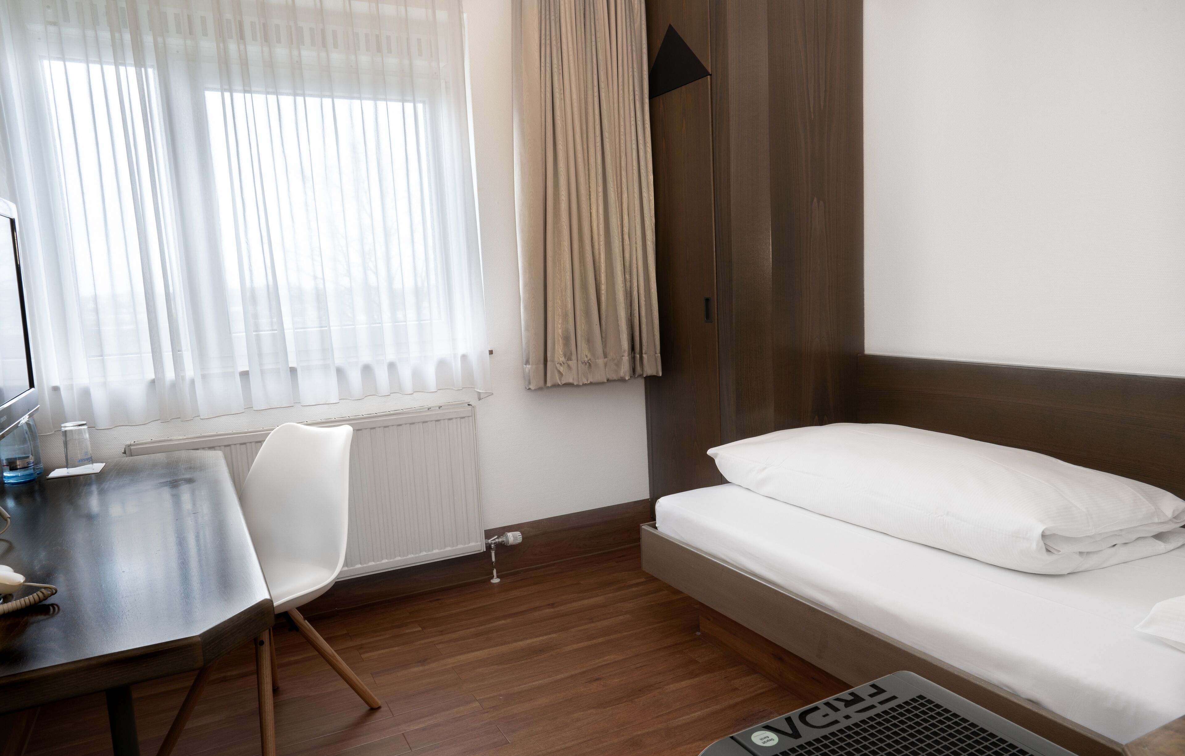 A hotel room with a bed, a desk, a chair, and a radiator.