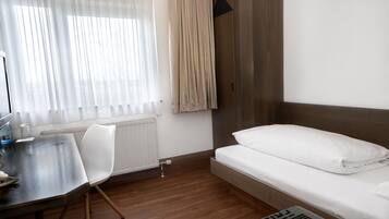 A hotel room with a bed, a desk, a chair, and a radiator.
