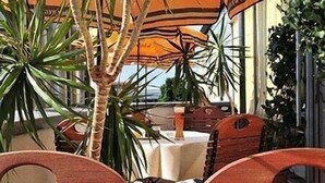 An outdoor seating area with wooden chairs and tables, surrounded by potted plants and umbrellas. - eXo Individual Hotel Heilbronn (Heilbronn)