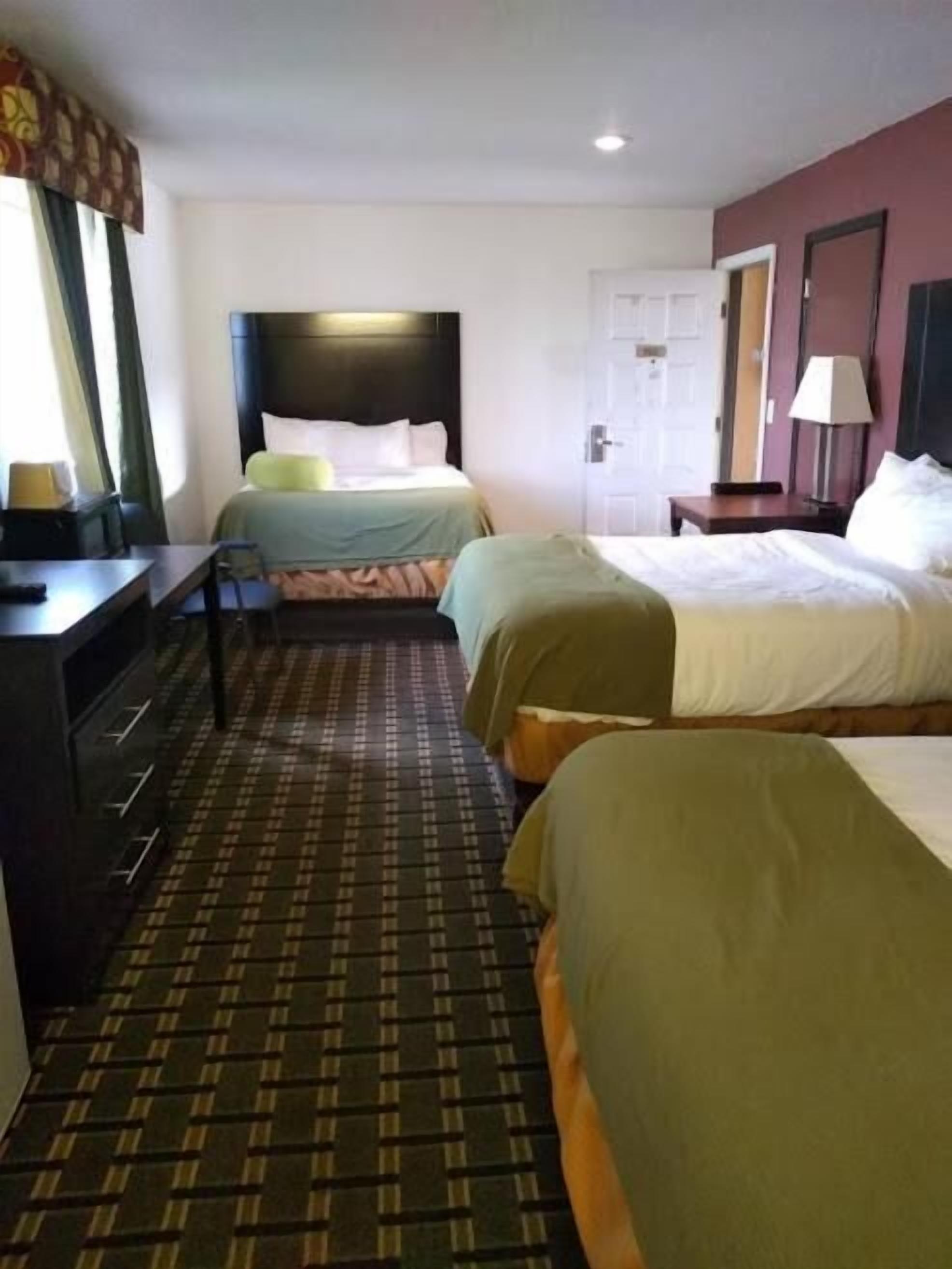 A hotel room with two beds, a desk, a chair, a wardrobe, and a patterned carpet.