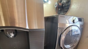 Un lavadero compacto con lavadora y secadora Samsung, un ventilador pequeño y una encimera blanca.
