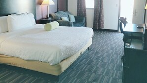 Habitación de hotel con una cama grande, un escritorio, una silla, una lámpara y un ventanal con cortinas.