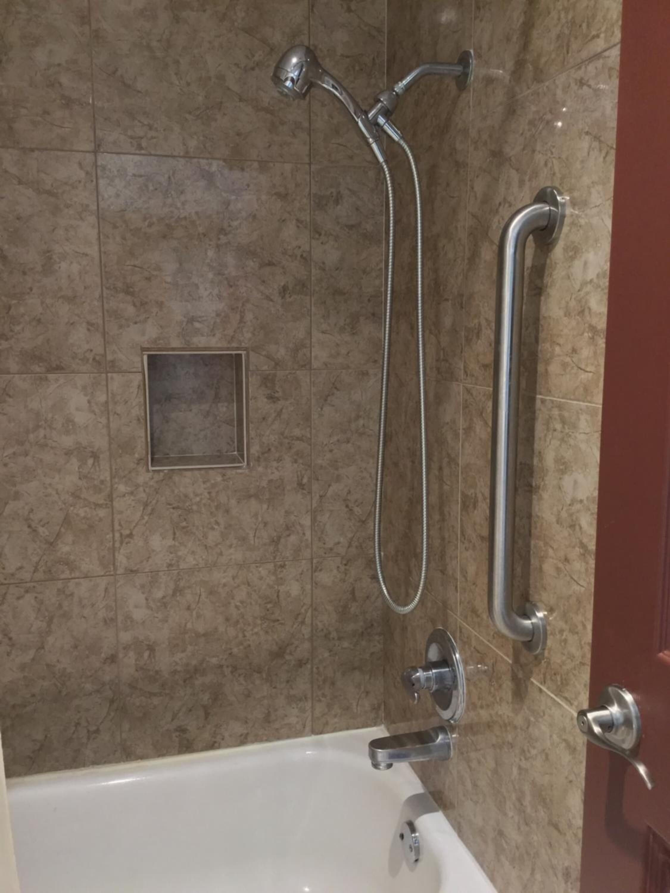 A bathroom with a bathtub, a showerhead, and a grab bar.