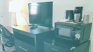 Una habitación de hotel compacta con escritorio, televisión, microondas y una silla.