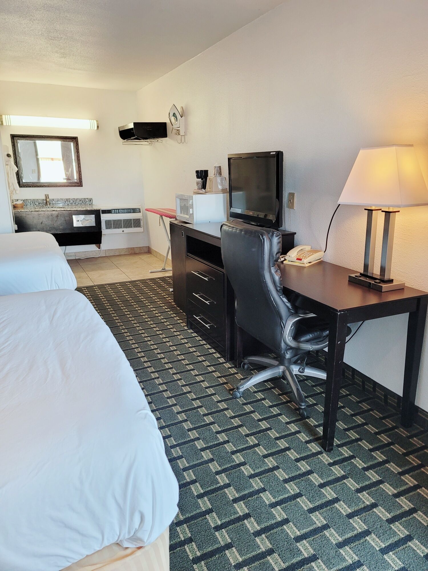 A hotel room with a bed, a desk with a computer, a telephone, and a lamp.