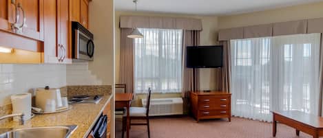 A hotel room with a kitchen area, a dining table, a TV, and a sofa.