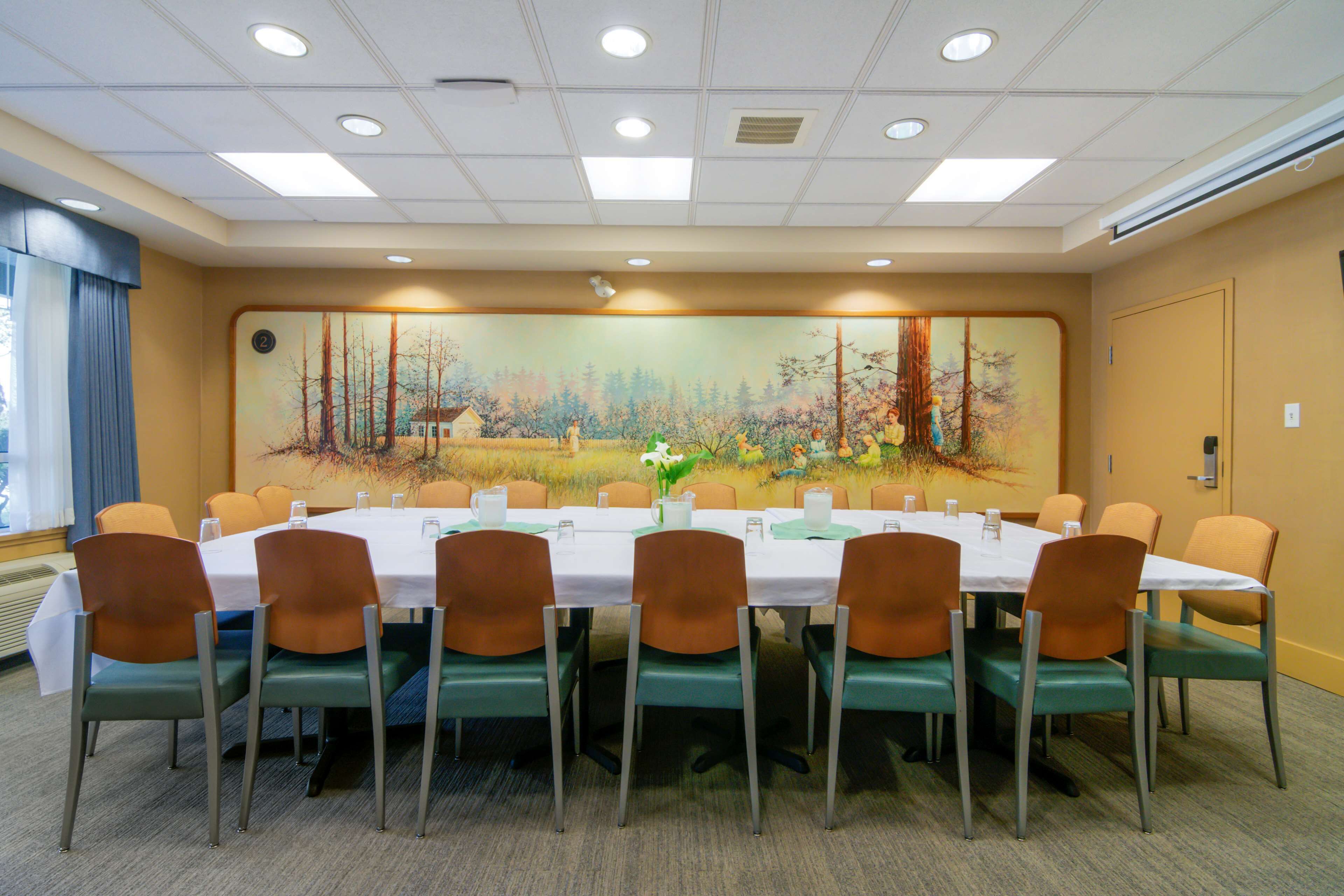 A conference room with a long table, multiple chairs, and a large mural on the wall.
