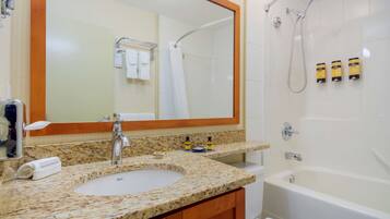 A bathroom with a granite countertop sink, a large mirror, a shower, and a bathtub.