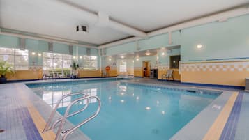 An indoor swimming pool with clear water, tiled floor, and metal pool ladders.
