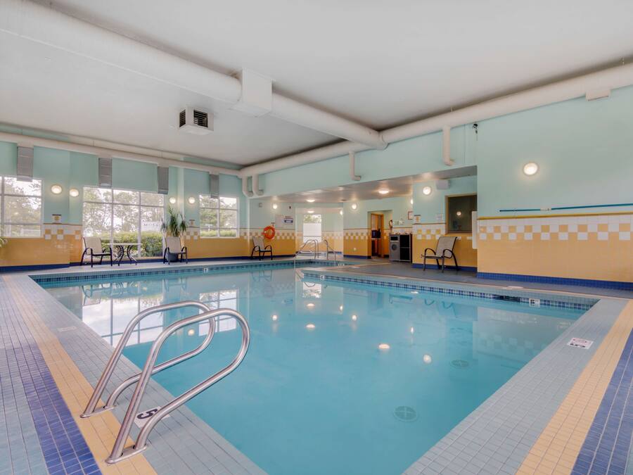 An indoor swimming pool with clear water, tiled floor, and metal pool ladders.