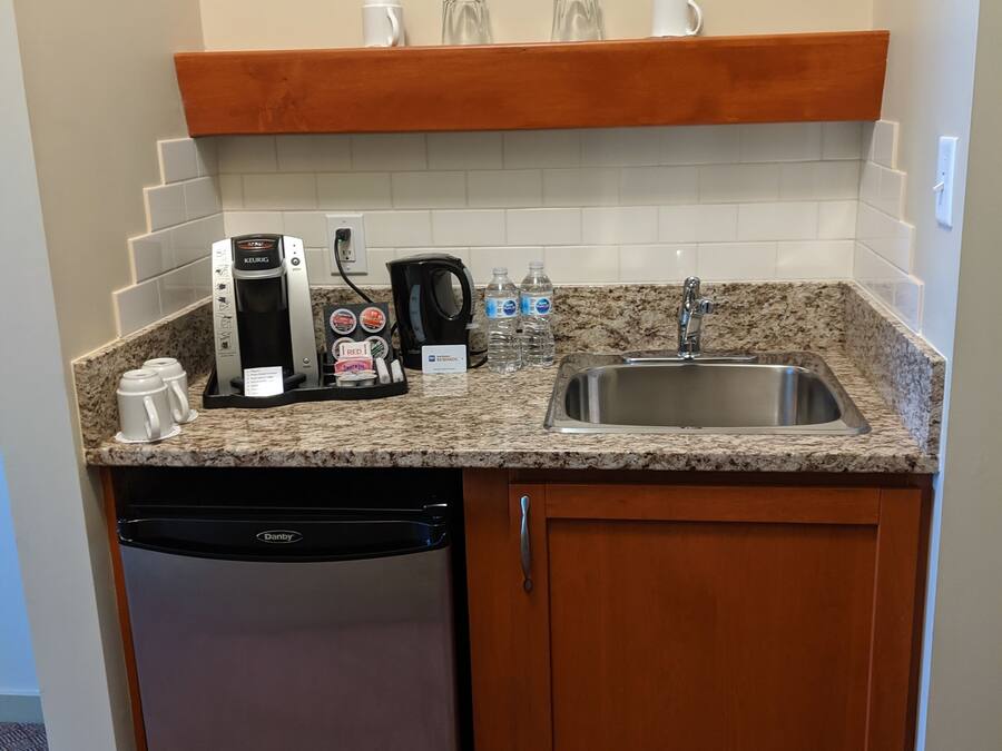 A compact kitchenette with a coffee maker, kettle, and water bottles.