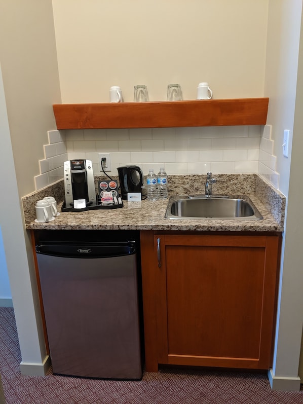 A compact kitchenette with a coffee maker, kettle, and water bottles.