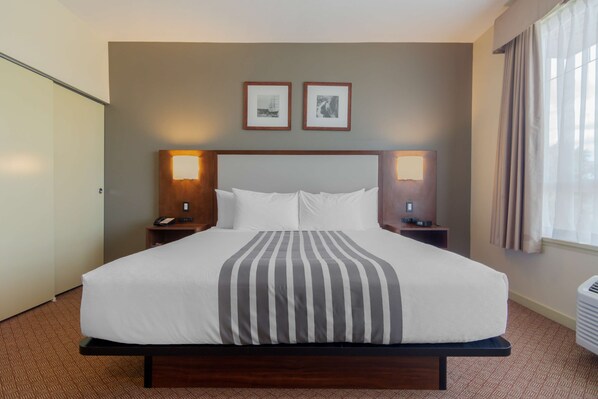 A hotel room with a large bed, two bedside tables with lamps, a headboard, and two framed pictures on the wall.