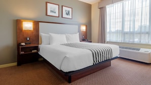 A hotel room with a large bed, two bedside tables, a nightstand, a wall-mounted air conditioner, and two framed pictures on the wall. - Best Western Plus Chemainus Inn (Chemainus)