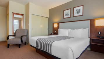 A hotel room with a large bed, a chair, a desk, and two framed pictures on the wall.
