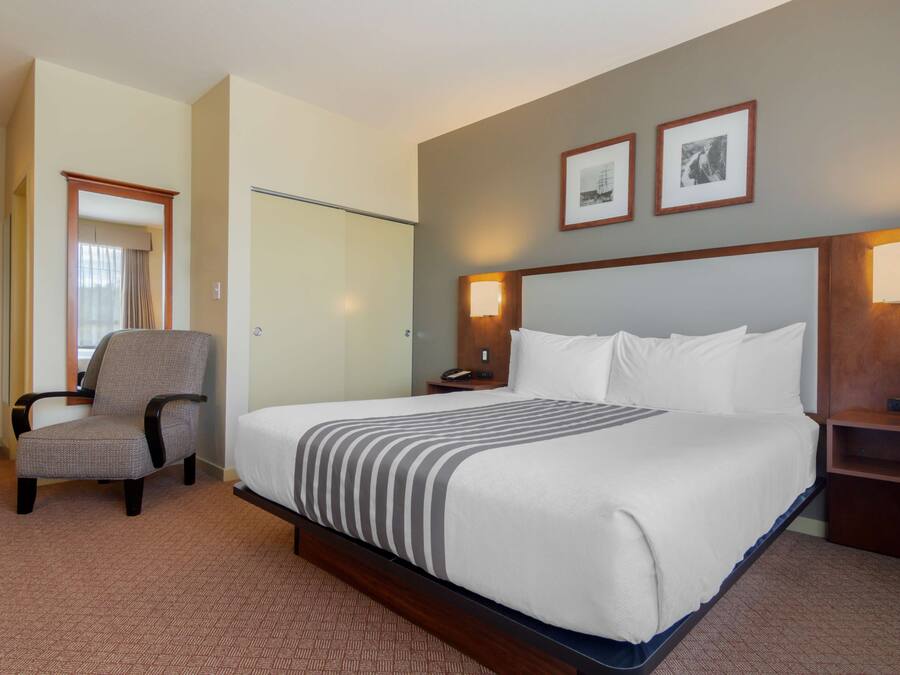 A hotel room with a large bed, a chair, a desk, and two framed pictures on the wall.
