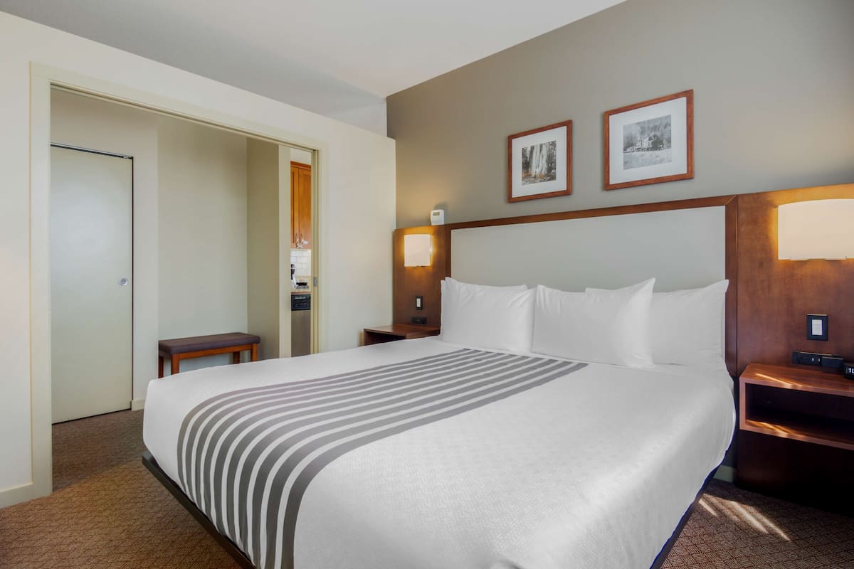 Une chambre d’hôtel avec un grand lit, une table de chevet, une commode, une porte et deux tableaux encadrés au mur.