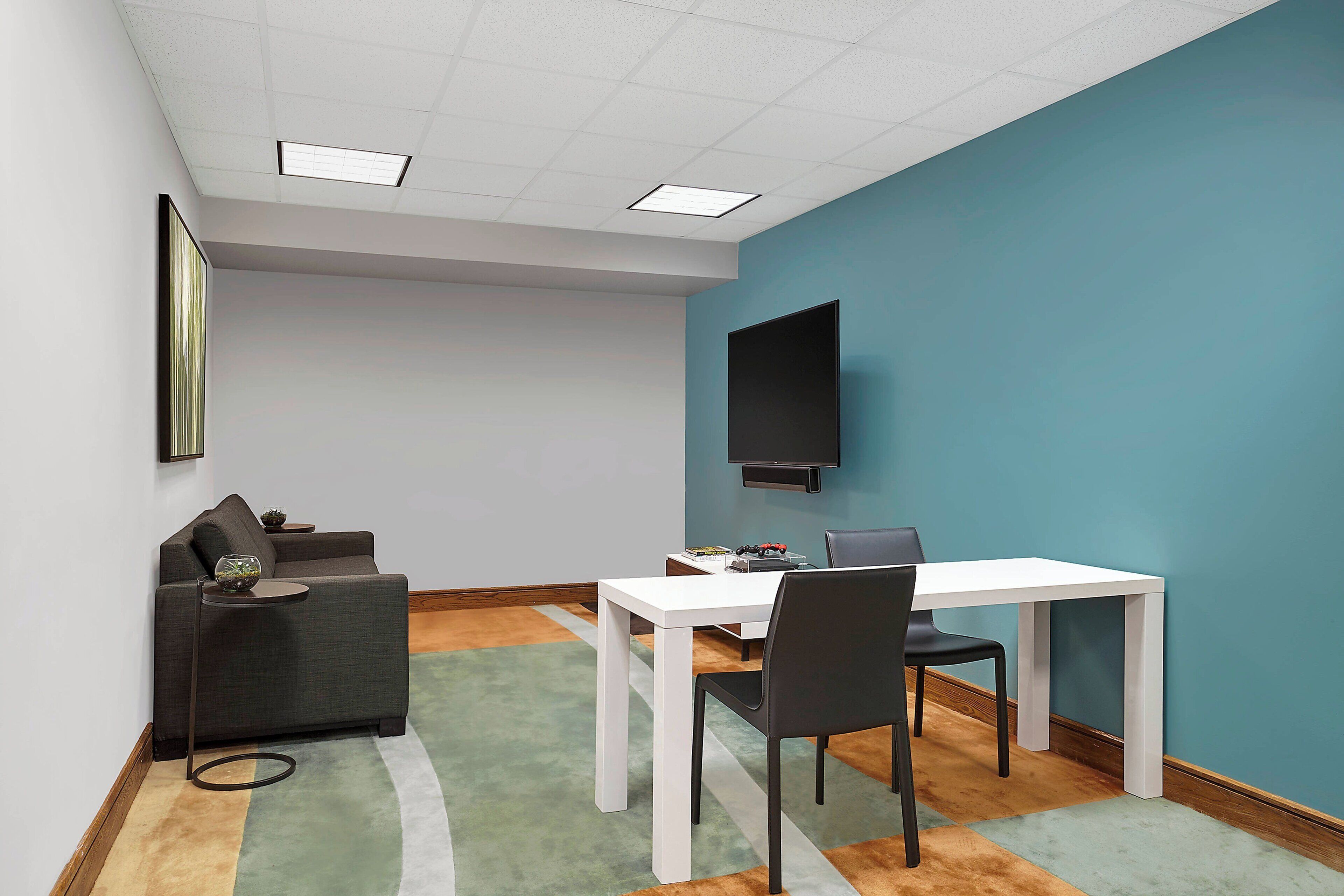 A conference room with a white table, black chairs, a grey sofa, and a blue accent wall.