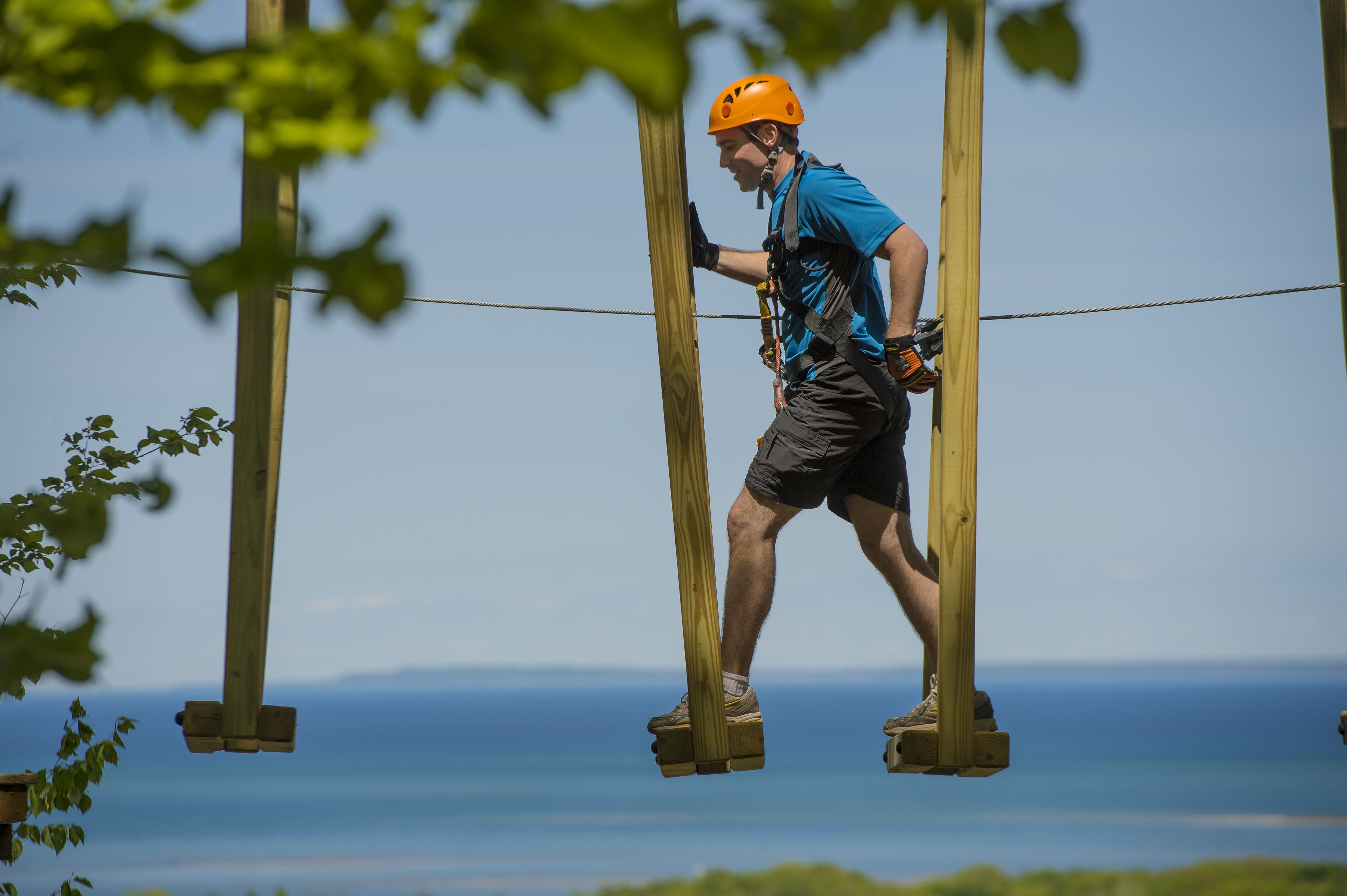 A person on a suspended zip line with a clear view of the ocean in the background.
