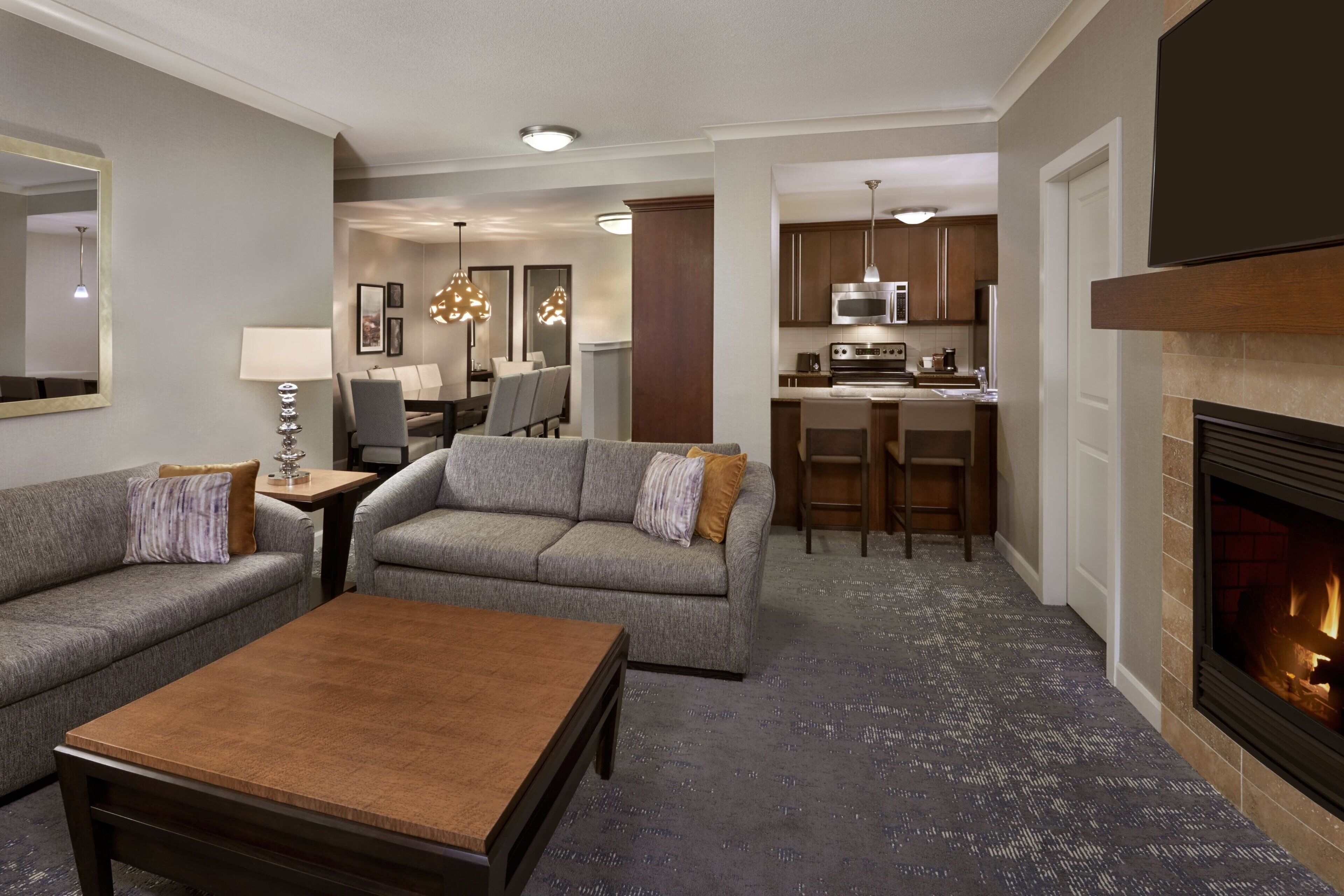 A modern living room with a fireplace, a dining area, and a kitchen.