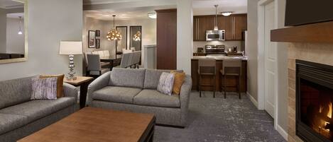 A modern living room with a fireplace, a dining area, and a kitchen.