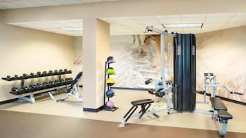 Un gimnasio con equipo de levantamiento de pesas, mancuernas y pelotas de ejercicio.