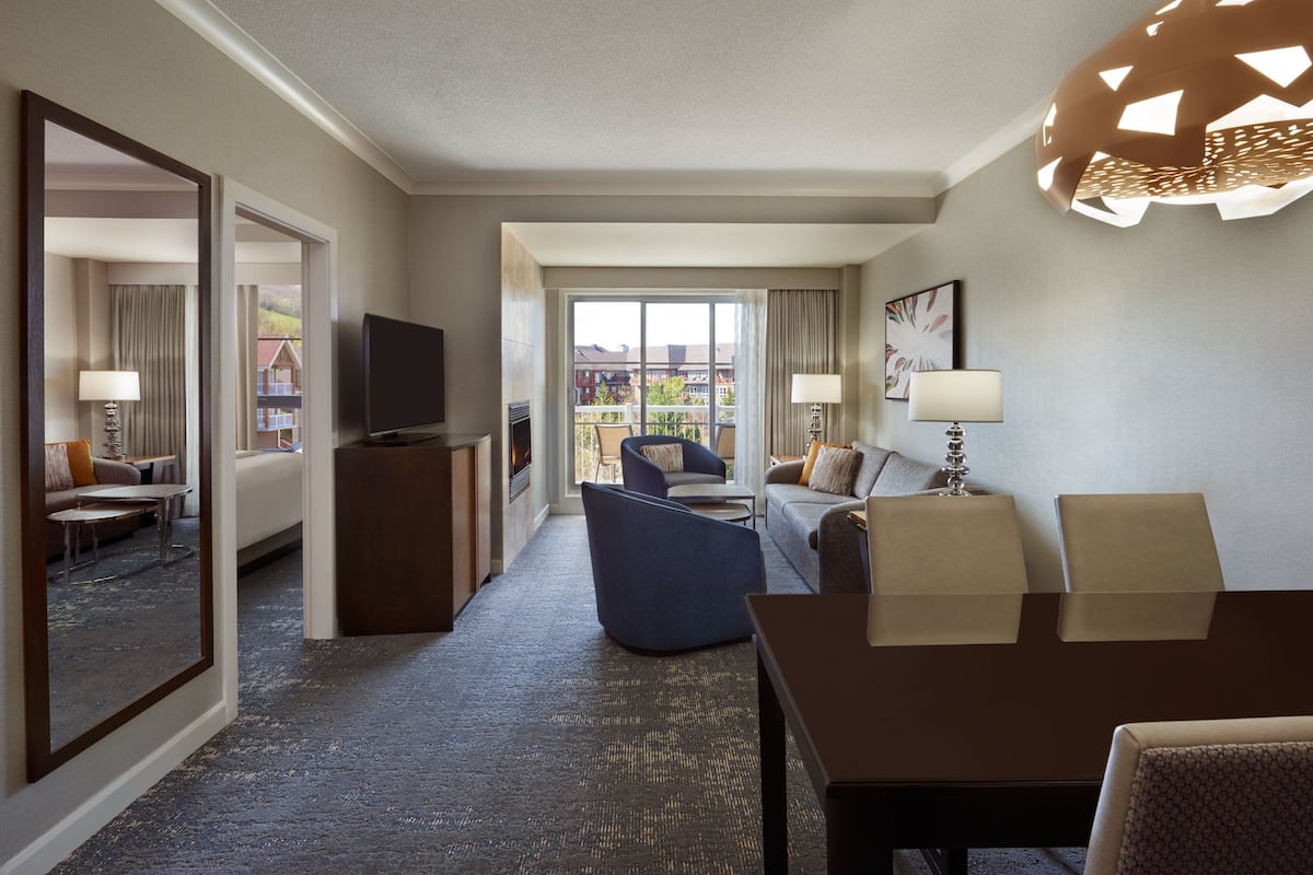 A hotel room with a living area, a dining table, a TV, and a balcony with a view of buildings.