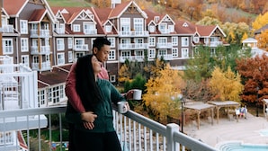 Una pareja en un balcón con vista a un hotel de varios pisos y un área de piscina.