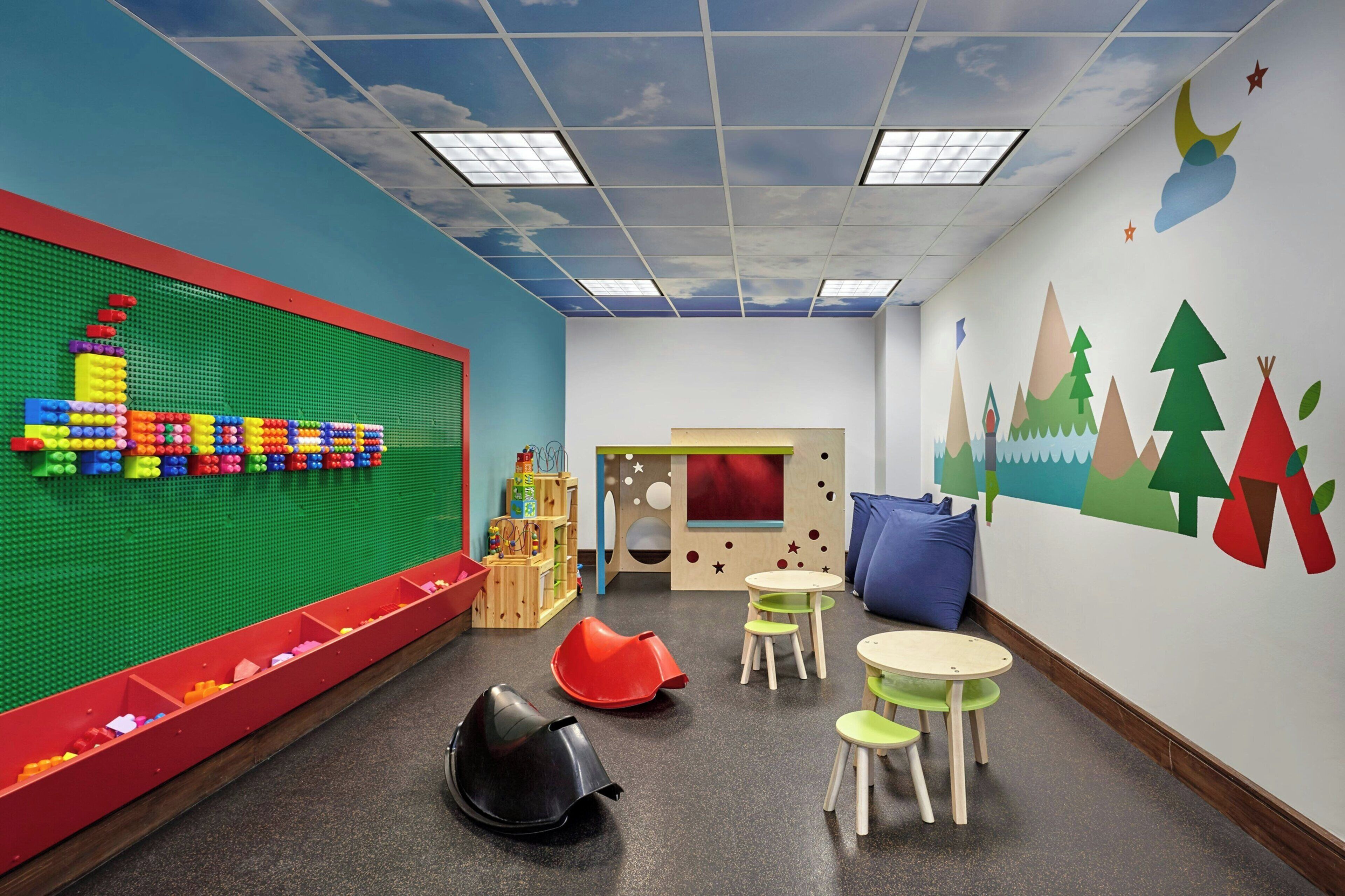 A children's playroom with a green wall, colorful play structures, and a mural of trees and mountains.