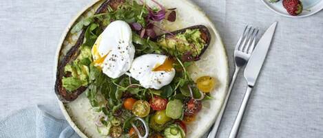 Un plato de ensalada con huevos pochados, tomates cherry y vegetales verdes.